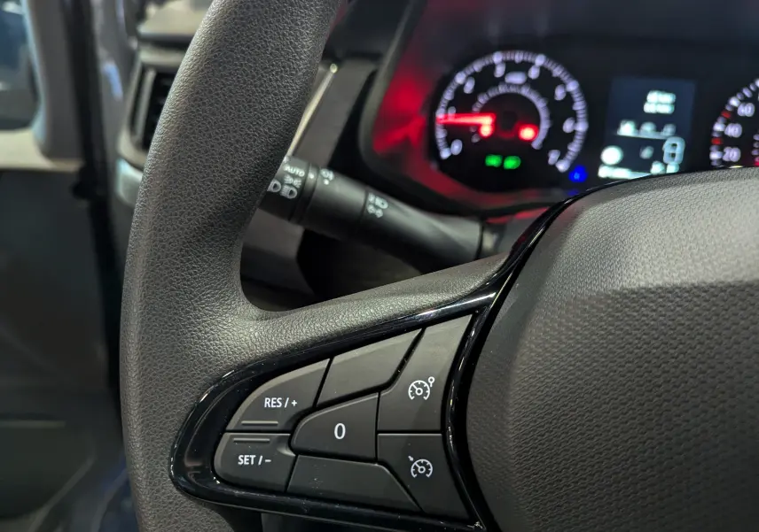 Gros plan sur les commandes de régulateur de vitesse au volant du Renault Trafic Fourgon gris urbain, tableau de bord en arrière-plan.