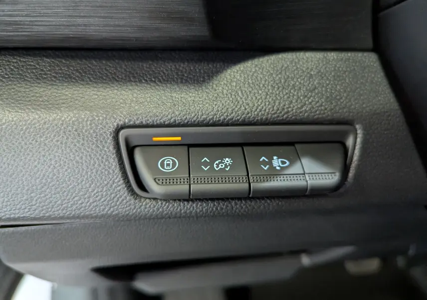 Gros plan sur les commandes de réglage des phares et verrouillage, tableau de bord noir du Renault Trafic Fourgon gris urbain.