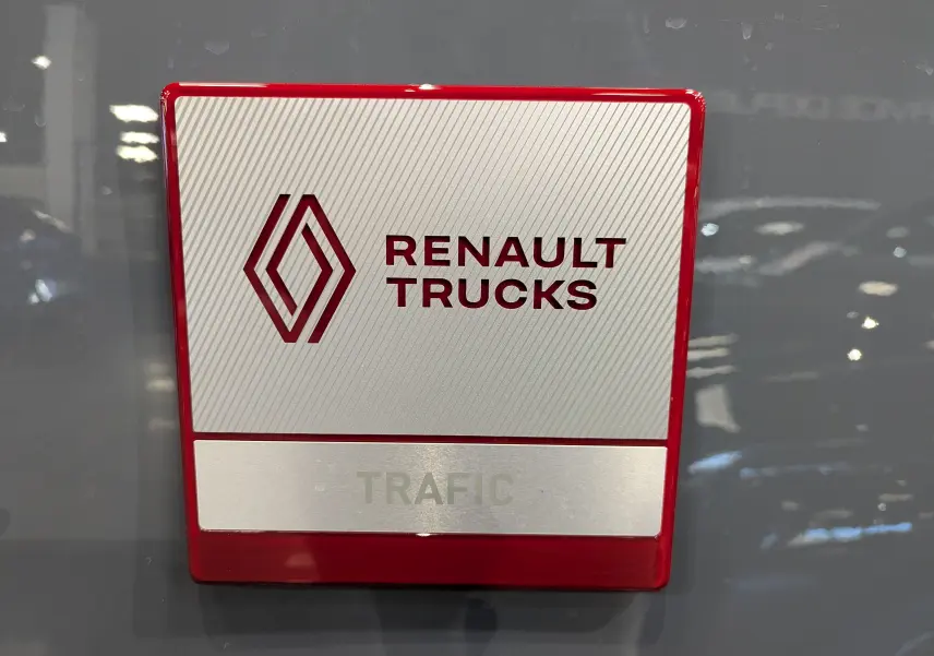 Gros plan sur le logo Renault Trucks rouge et argent fixé sur la carrosserie gris urbain du Trafic Fourgon.