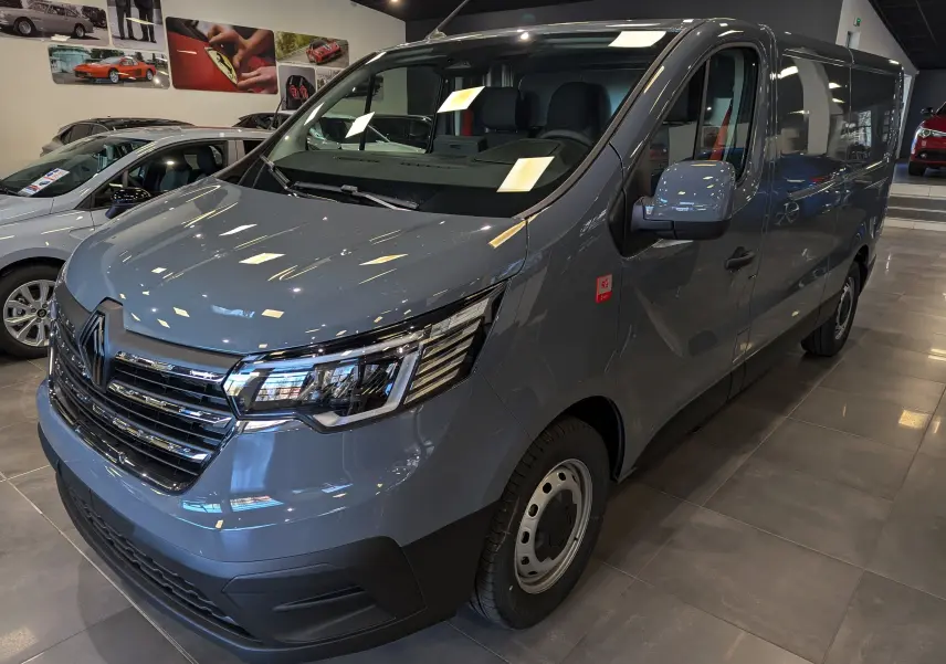 Renault Trafic Fourgon gris urbain en vue 3/4 avant droit dans un showroom, avec calandre chromée et phares LED.