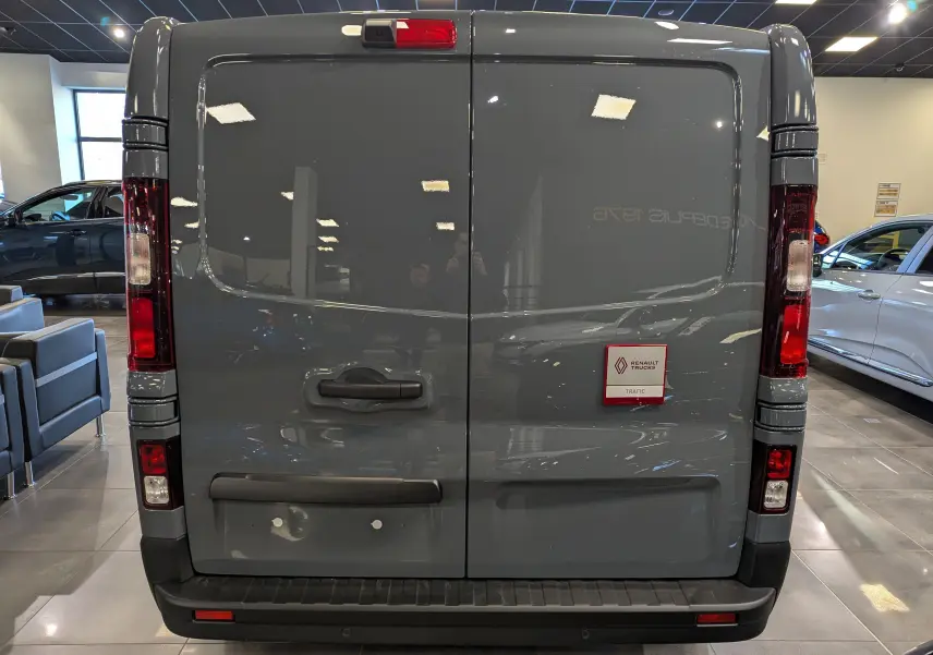 Vue arrière du Renault Trafic Fourgon gris urbain 2025, portes battantes fermées avec feux verticaux et logo Renault Trucks.