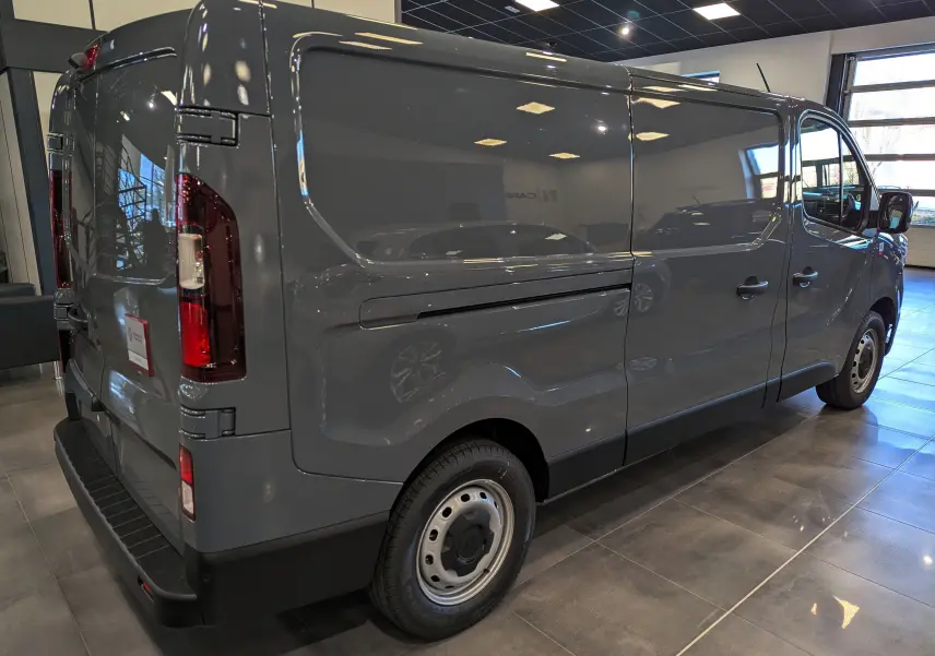Renault Trafic Fourgon gris urbain vu en 3/4 arrière droit dans un showroom lumineux avec portes latérales fermées.