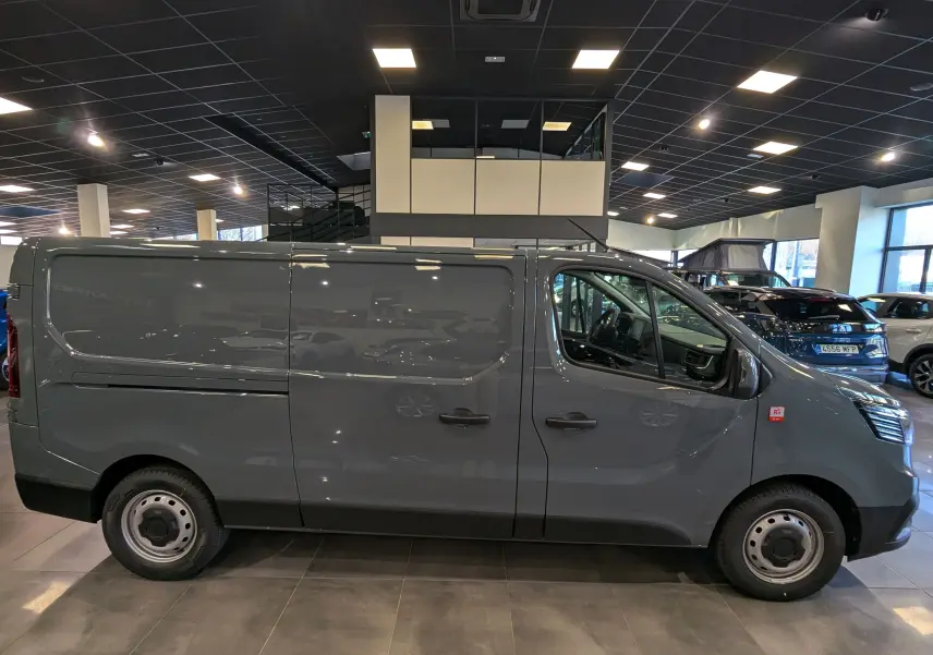 Renault Trafic Fourgon L2H1 2025 gris urbain vu de profil côté droit dans un showroom lumineux.