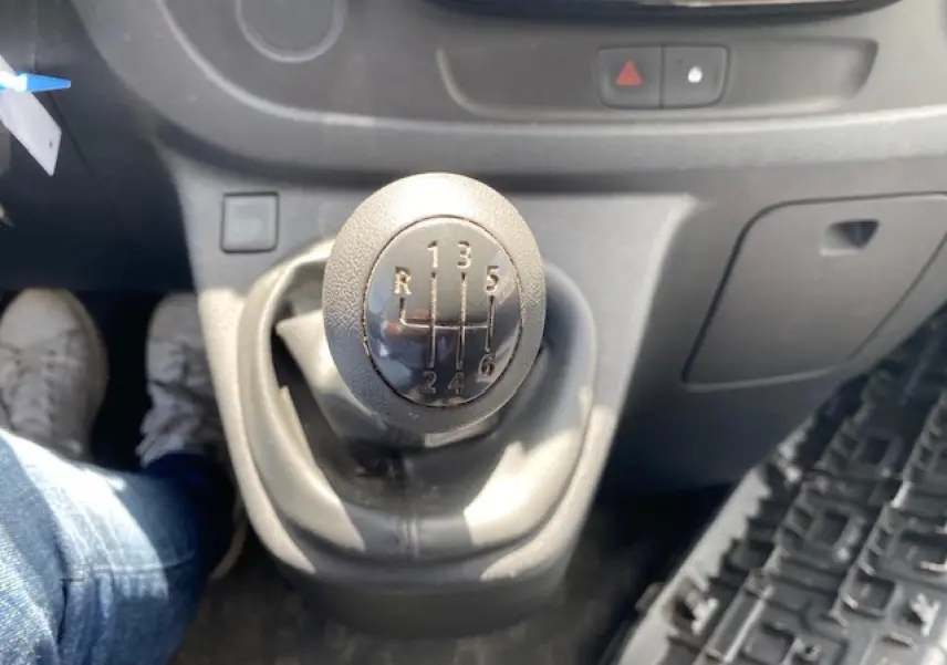 Gros plan sur le levier de vitesses manuel noir de l'Opel Vivaro blanc, avec tableau de bord gris en arrière-plan.