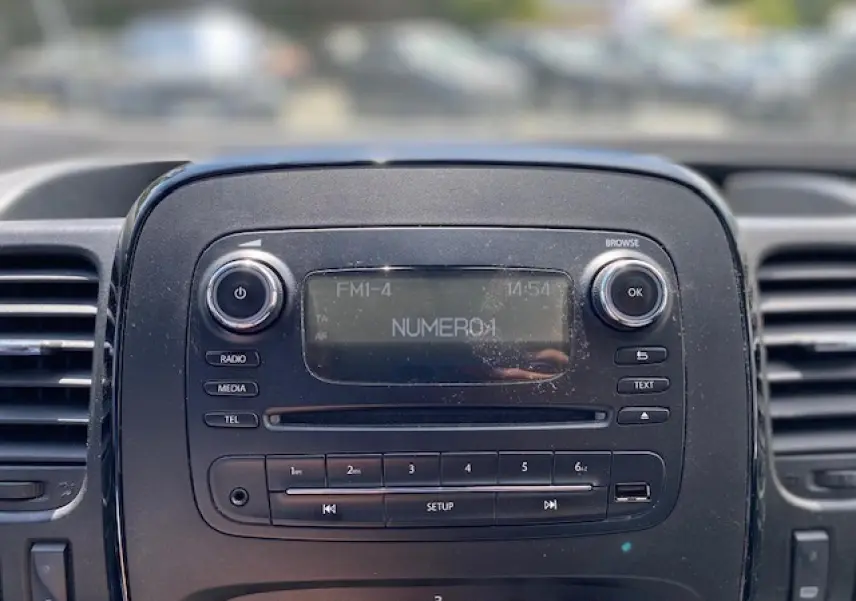 Gros plan sur la console centrale noire de l'Opel Vivaro blanc, affichant la radio FM et les commandes multimédia.