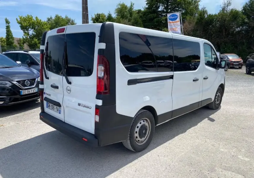 Vue 3/4 arrière droite d'un Opel Vivaro blanc, combi rallongé avec vitres teintées et portes arrière battantes.