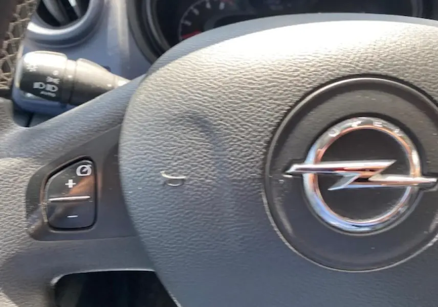 Gros plan sur le volant noir avec logo Opel en relief et commandes de régulateur de vitesse visibles sur la gauche.