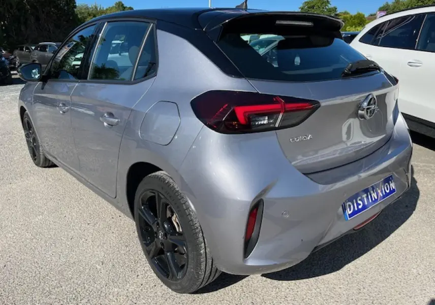 Vue 3/4 arrière droite d'une Opel Corsa gris métallisé avec toit noir et jantes noires sur un parking extérieur.