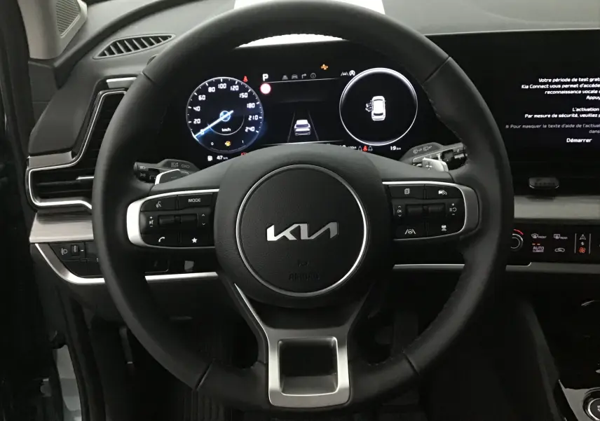 Vue rapprochée du volant noir du Kia Sportage 2025 avec combiné digital 12,3 pouces et écran tactile à droite.