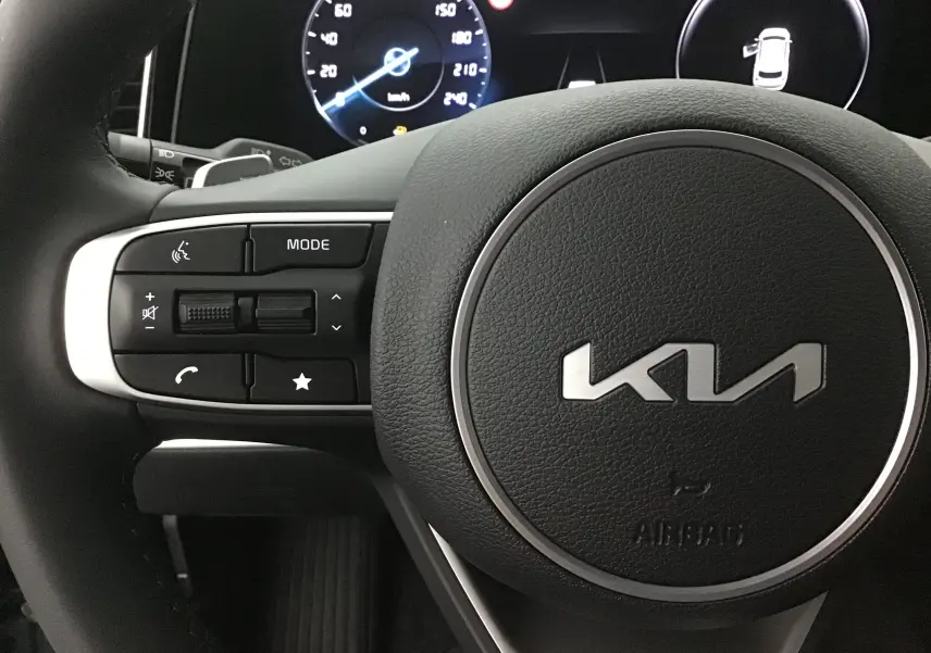 Gros plan sur le volant cuir noir du Kia Sportage 2025 avec commandes multifonctions et tableau de bord digital lumineux.