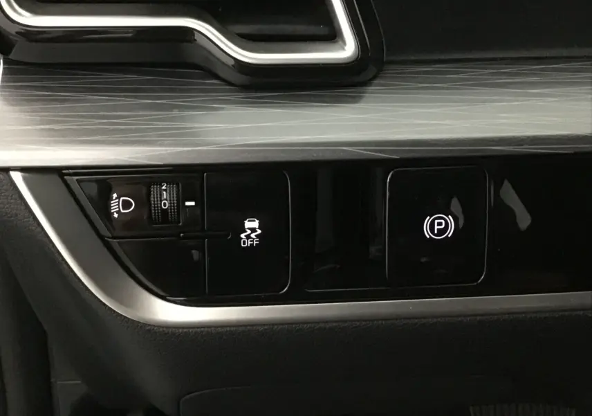 Détail du tableau de bord du Kia Sportage gris Sirius 2025 montrant les commandes d'éclairage et frein à main électronique.