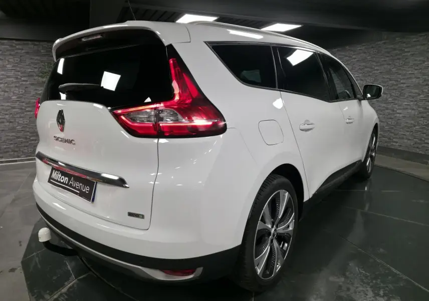 Vue 3/4 arrière droite du Renault Scénic blanc nacré avec jantes alliage et attelage visible en intérieur sombre.