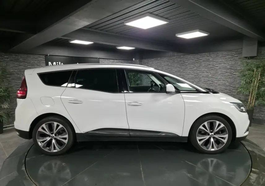Profil côté gauche d’un Renault Scénic blanc nacré 2017 avec jantes alliage et vitres surteintées en intérieur showroom.