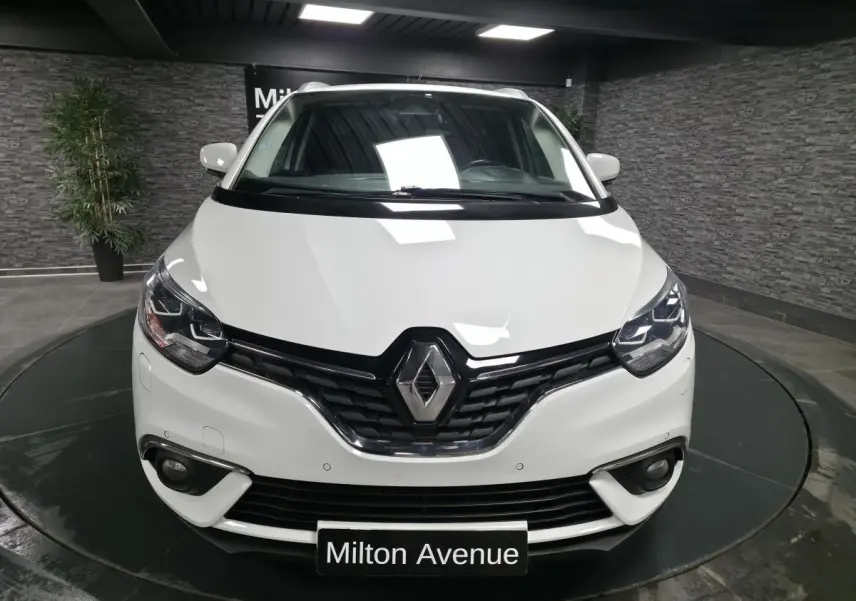 Vue de face d'un Renault Scénic blanc nacré 2017 avec calandre chromée et phares LED dans un showroom.