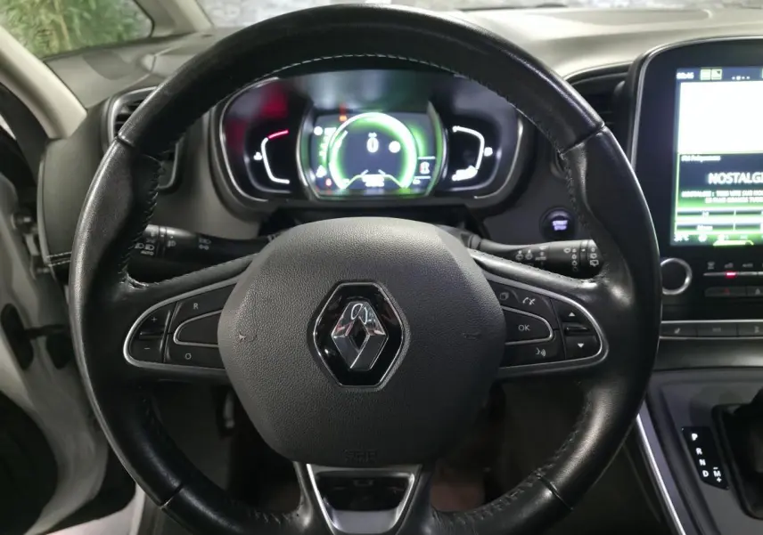 Vue rapprochée du volant cuir noir avec logo Renault, tableau de bord numérique et écran multimédia du Scenic blanc 2017.