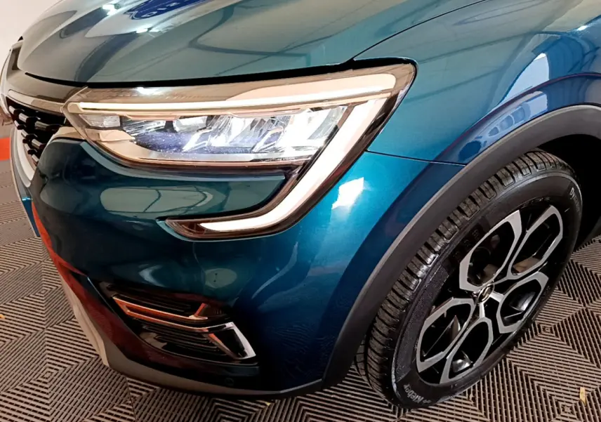 Gros plan sur l'avant droit bleu du Renault Arkana 2023, mettant en valeur le phare LED et la roue au design moderne.