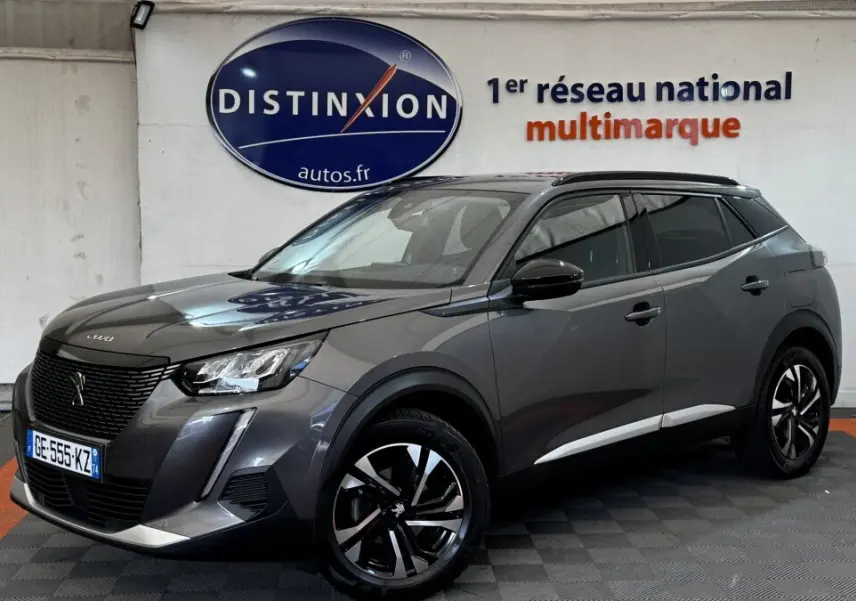 Peugeot 2008 gris foncé vue en 3/4 avant droit, avec jantes noires et toit panoramique visible en intérieur showroom.