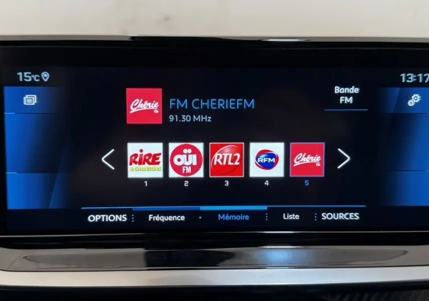 Écran tactile central de la Peugeot 2008 gris foncé affichant les stations radio FM en interface moderne.