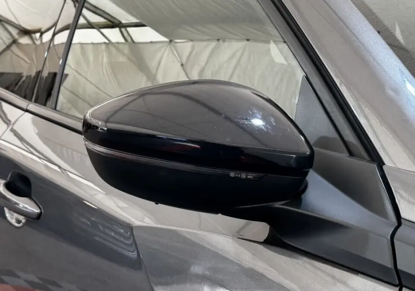 Gros plan sur le rétroviseur droit noir brillant du Peugeot 2008 gris foncé, avec poignée de porte visible.