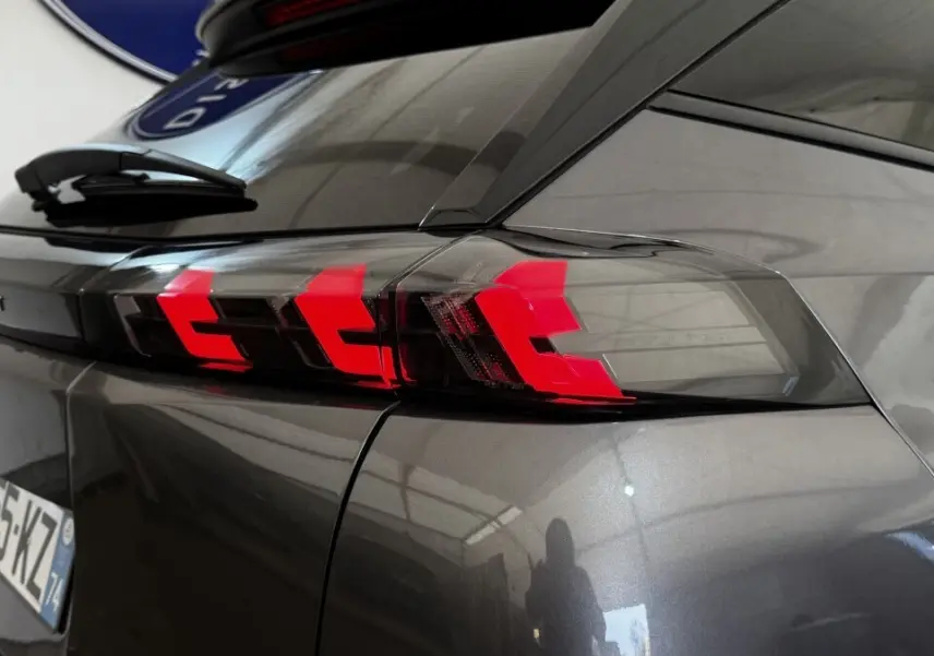 Gros plan sur le feu arrière droit rouge vif d’un Peugeot 2008 gris foncé, avec reflet sur la carrosserie lisse.