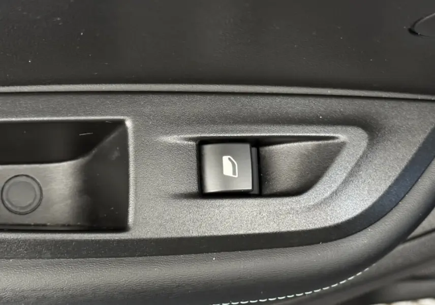 Bouton de commande de vitre électrique sur la porte intérieure noire d'un Peugeot 2008 gris foncé, vue rapprochée.