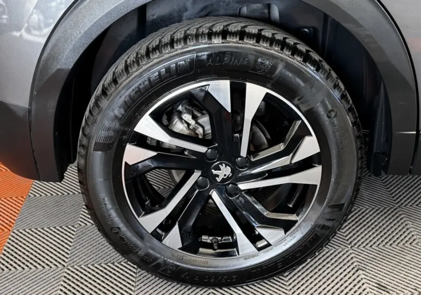 Gros plan sur la roue arrière droite gris foncé d’un Peugeot 2008 avec jante alliage noir et argent et pneu Michelin Alpine.