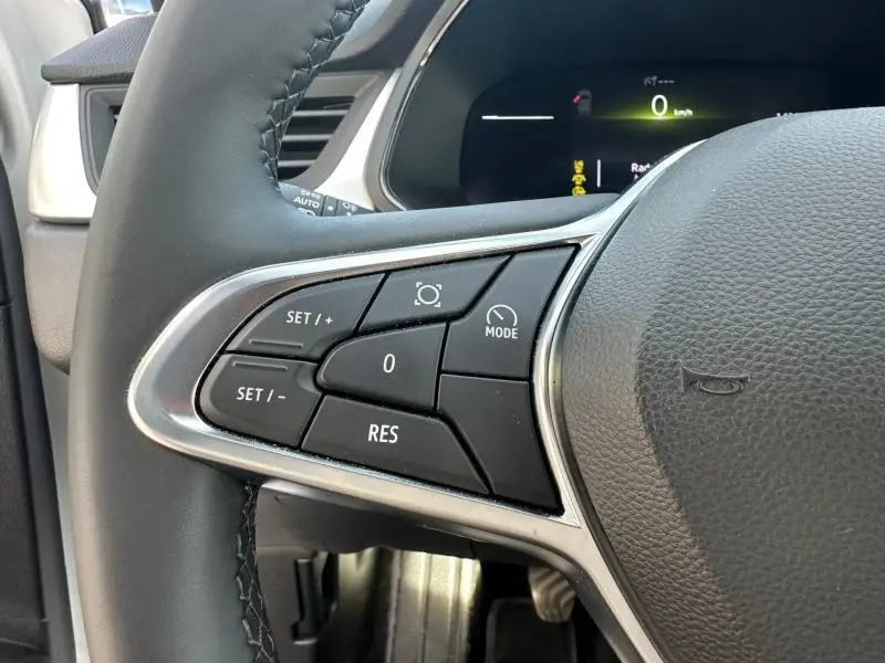 Gros plan sur les commandes de régulateur de vitesse à gauche du volant noir du Renault Captur blanc nacré 2025.