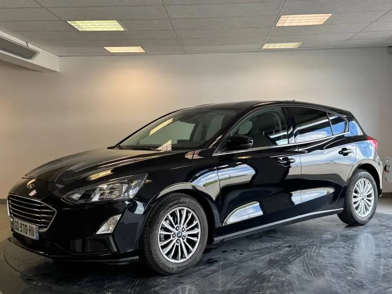 Ford Focus noir Agate métallisé vue 3/4 avant droit dans un intérieur lumineux avec calandre chromée.