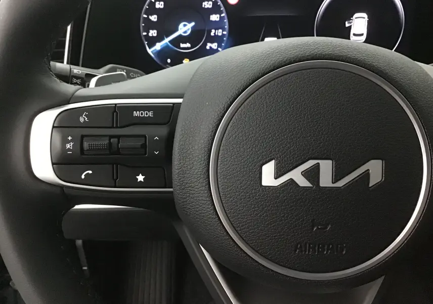 Gros plan sur le volant cuir noir du Kia Sportage 2025 avec commandes intégrées et tableau de bord digital lumineux.