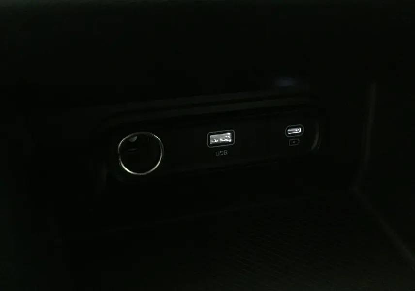 Prise USB et port allume-cigare dans l'habitacle sombre du Kia Sportage gris Sirius 2025.