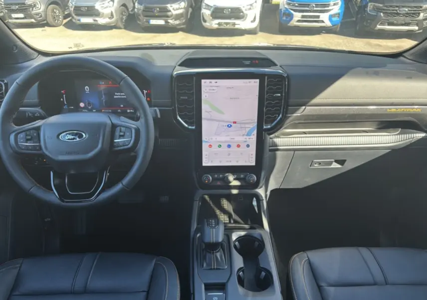 Intérieur du Ford Ranger Wildtrak 2025 en vue frontale, tableau de bord noir avec écran tactile vertical et volant multifonction.