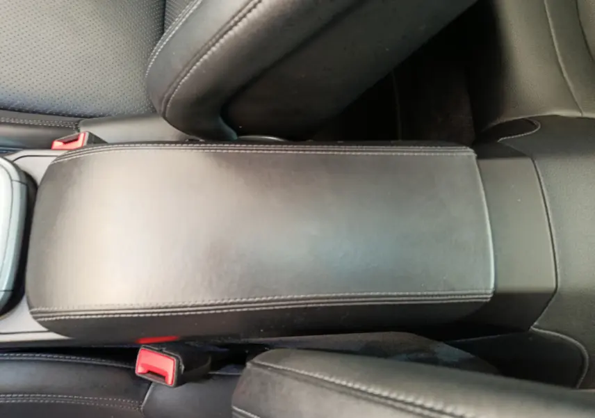 Vue rapprochée de l'accoudoir central en cuir noir et des ceintures de sécurité rouges à l'intérieur d'une Porsche 911 Carrera 4S Coupé gris foncé.