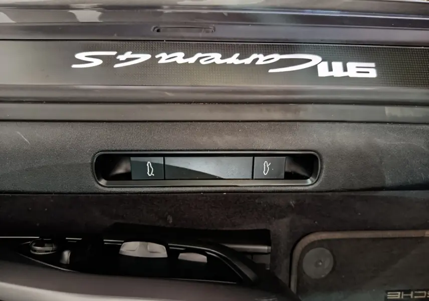 Détail intérieur montrant la poignée d'ouverture du coffre et la plaque Carrera 4S sur seuil noir d'une Porsche 911 gris foncé.