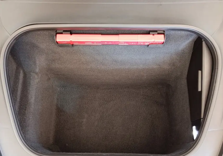 Coffre avant ouvert vu de dessus, intérieur gris foncé avec trousse de secours rouge visible sur le bord.