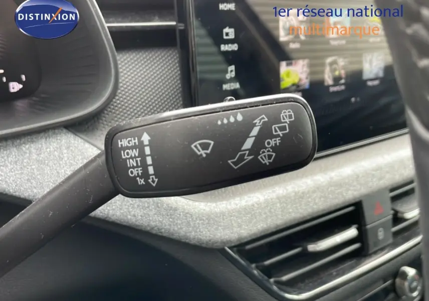 Gros plan sur la commande d’essuie-glace dans l’habitacle d’une Skoda Scala noir magique métal, avec écran tactile en arrière-plan.
