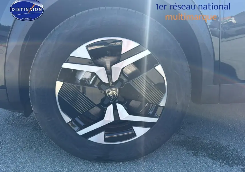 Gros plan sur la roue avant gauche noire avec jante alu au design moderne du Peugeot 2008 1.2 hybrid 145 allure 2025.