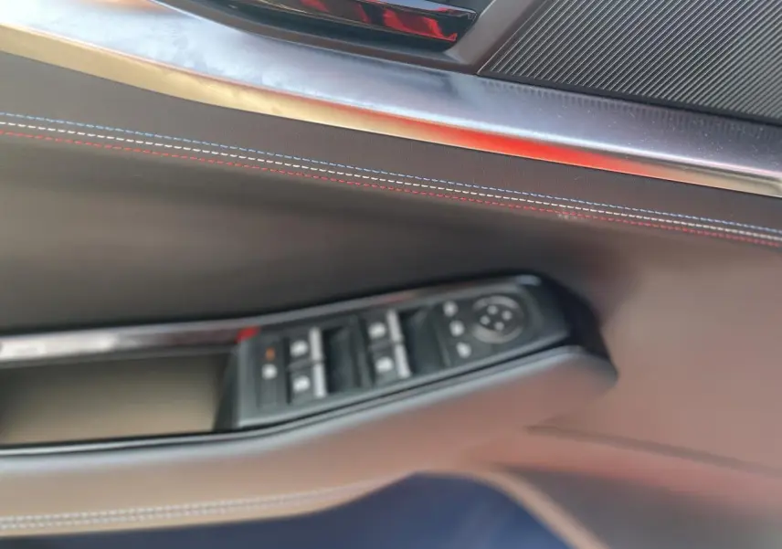 Détail de la porte côté gauche de la Renault Rafale 2025 rouge avec surpiqûres tricolores et commandes de vitres.