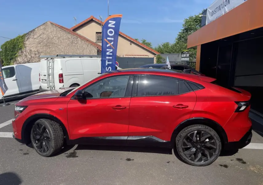 Profil côté gauche de la Renault Rafale rouge à toit noir, avec jantes noires et vitres teintées, stationnée en extérieur.