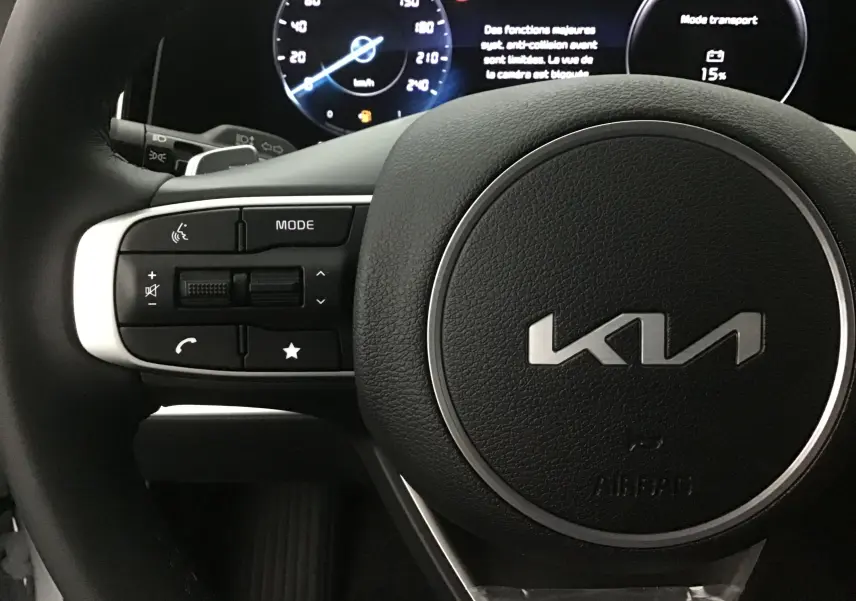 Gros plan sur le volant noir du Kia Sportage 2025 avec commandes intégrées et combiné d'instrumentation digital lumineux.
