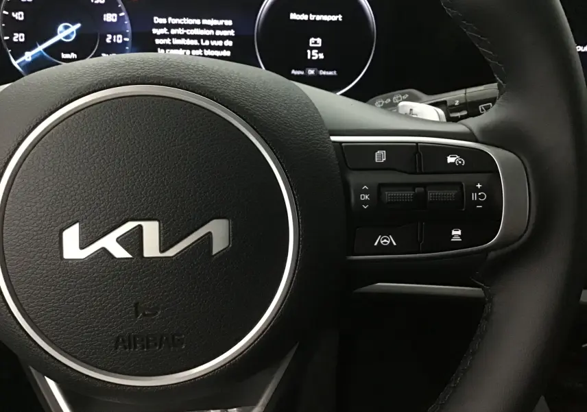 Gros plan sur le volant cuir du Kia Sportage 2025 avec commandes multifonctions côté droit et écran digital en arrière-plan.