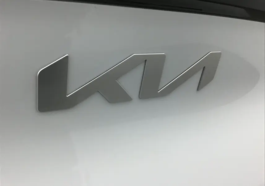 Gros plan sur l'emblème métallique KIA sur la carrosserie blanche du SUV Sportage 2025.