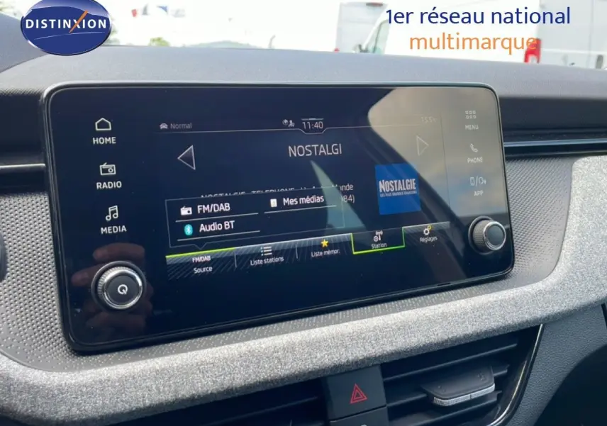 Écran tactile central du tableau de bord de la Skoda Scala blanc glacier, affichant la radio FM/DAB Nostalgie.