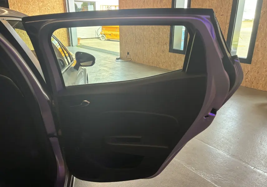 Vue intérieure de la porte arrière gauche ouverte d'une Renault Clio gris 2022, soulignant la poignée et la vitre.