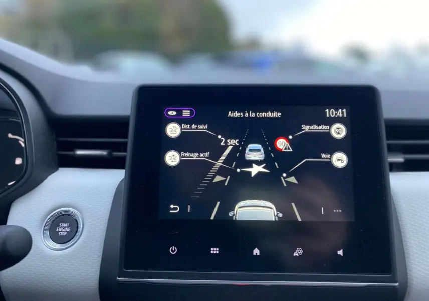 Écran tactile central de la Renault Clio 2023 affichant les aides à la conduite avec bouton démarrage visible à gauche.