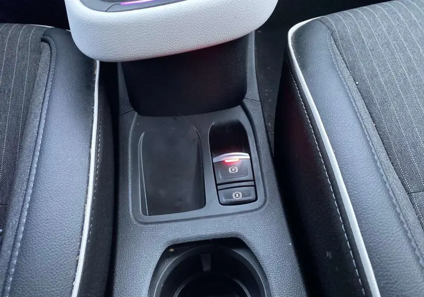 Gros plan sur la console centrale de la Renault Clio blanche 2023, montrant le frein à main électrique et les sièges noirs à surpiqûres blanches.