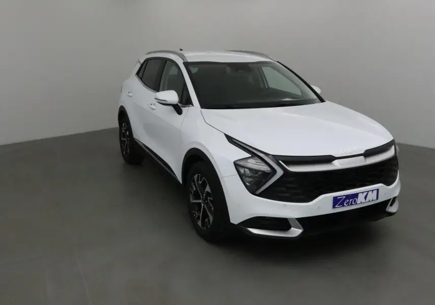Vue 3/4 avant d'un KIA SPORTAGE blanc 2025 avec calandre noire et jantes alliage noires et argentées.