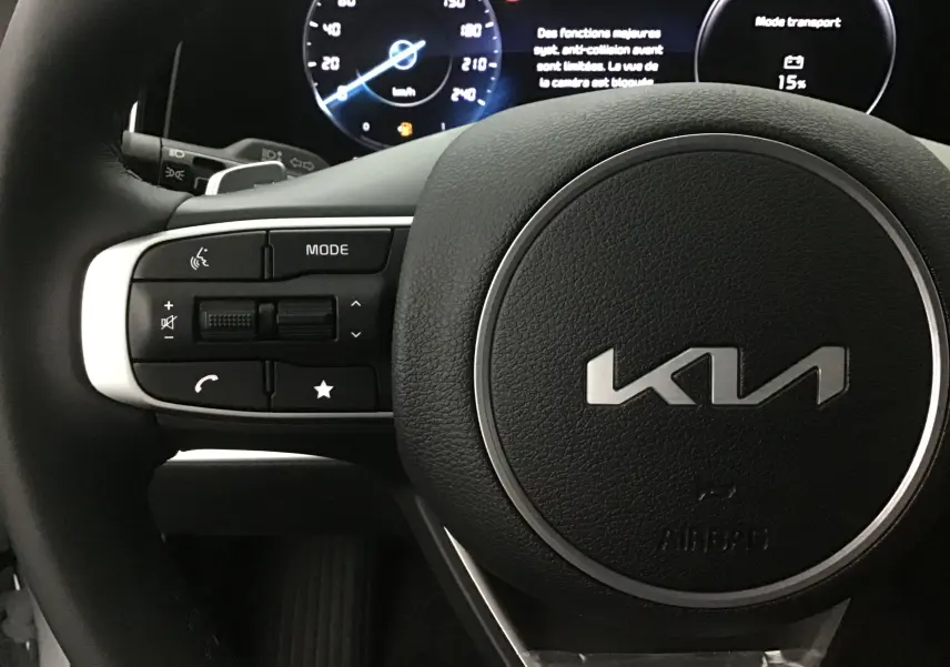 Gros plan sur le volant cuir noir du Kia Sportage 2025 avec commandes multifonctions et combiné digital lumineux.