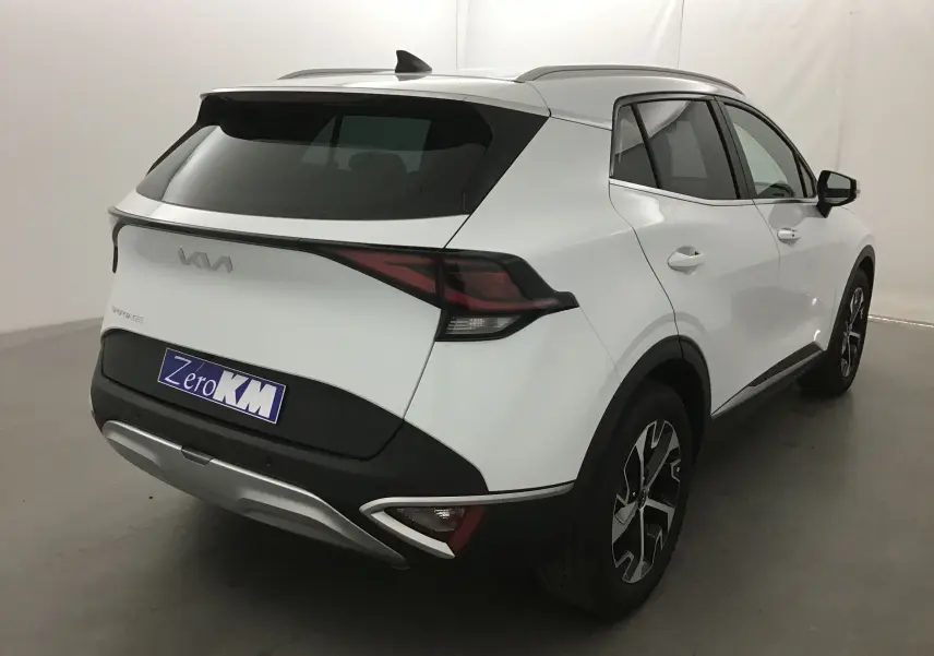 Vue 3/4 arrière droite du KIA SPORTAGE blanc 2025 avec feux arrière LED et jantes alliage noires et argentées.