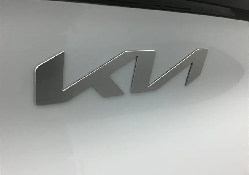 Gros plan sur l'emblème KIA en métal brossé sur la carrosserie blanche du SUV Sportage 2025.