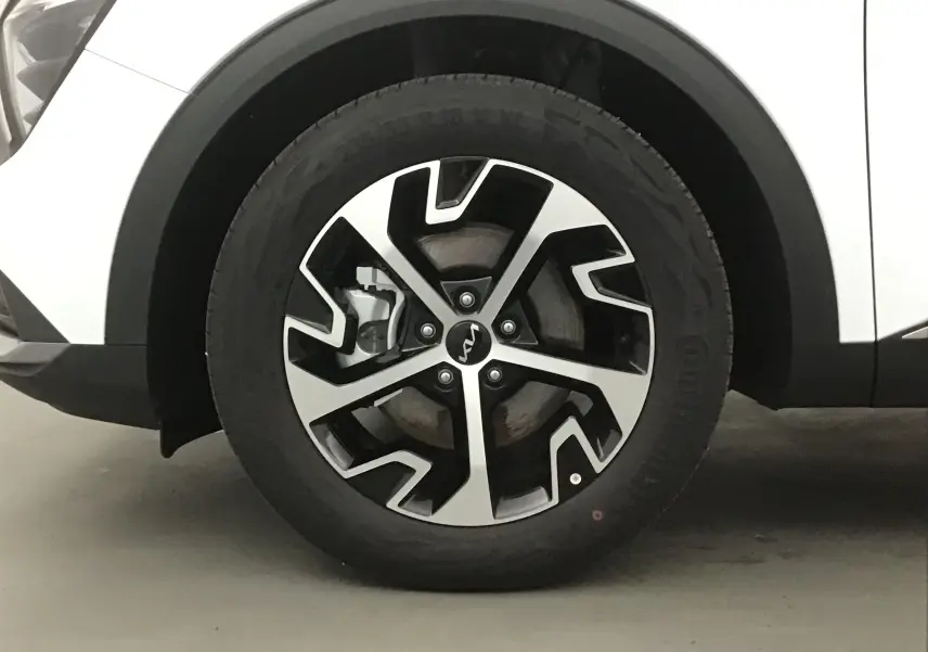 Gros plan sur la roue avant gauche du Kia Sportage blanc 2025, mettant en valeur la jante alliage bicolore au design moderne.